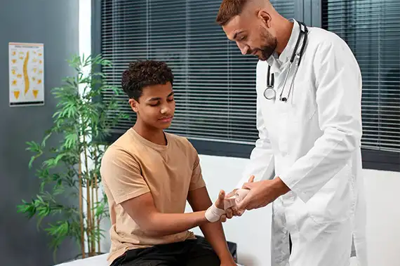 Medical professional bandaging a young patient's hand and assessing injury severity.