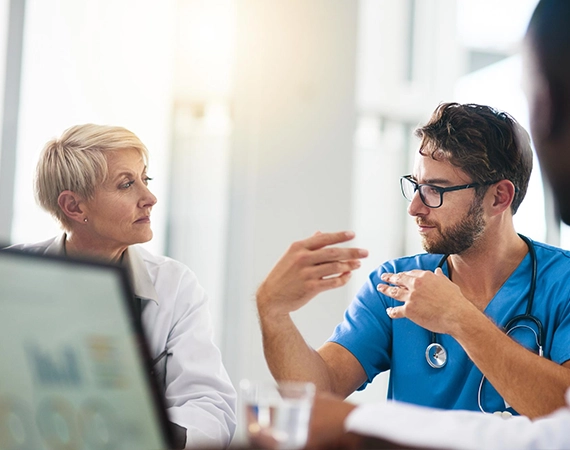 A doctor having a medical discussion with a colleague in a clinical setting.
