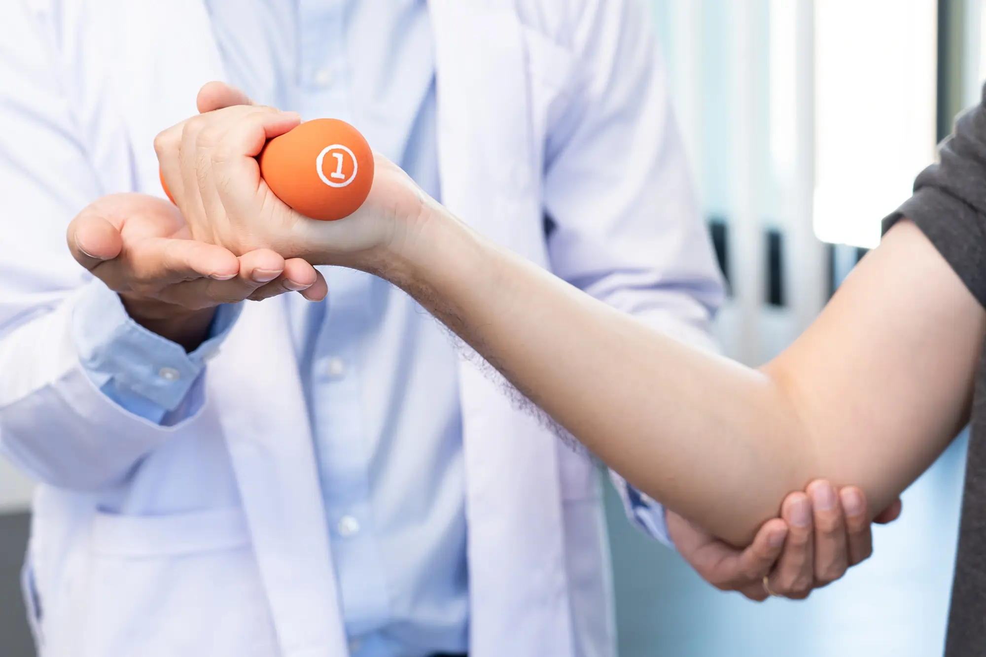 Doctor handing a soft ball to a patient with a broken arm for grip therapy while patient shows signs of pain.