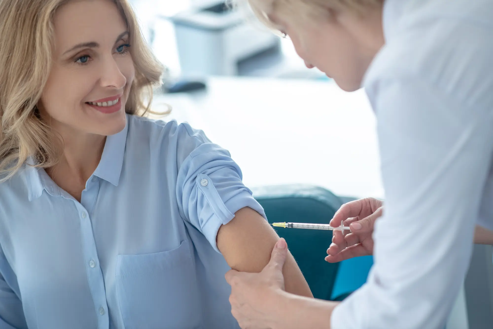 Doctor injecting a flu vaccine to a young woman during a clinical appointment.
