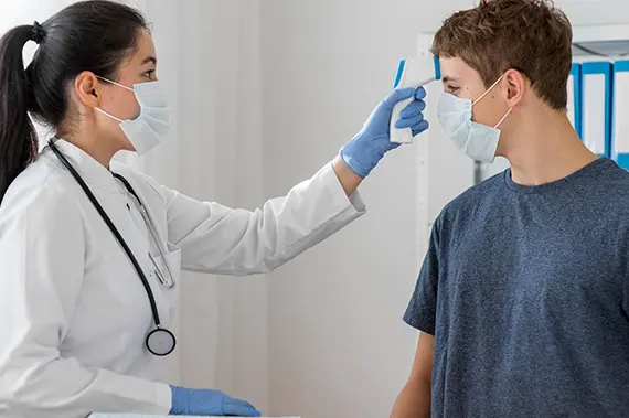 Doctor using a contactless thermometer to check a boy’s body temperature during a health exam.