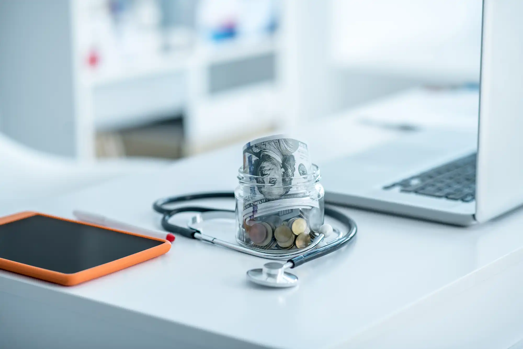 Dollar bills and coins placed beside a stethoscope on a doctor's desk, symbolizing affordable healthcare.