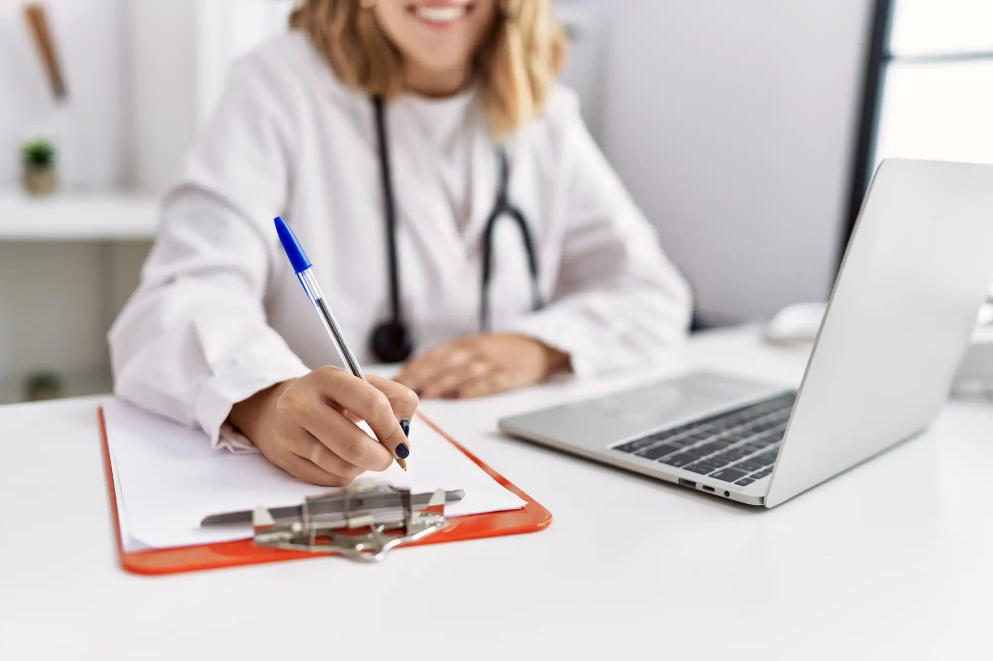 Healthcare provider using a laptop to update medical records during a patient consultation.