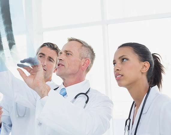 Team of doctors closely examining a patient’s chest X-ray for diagnosis and treatment planning.