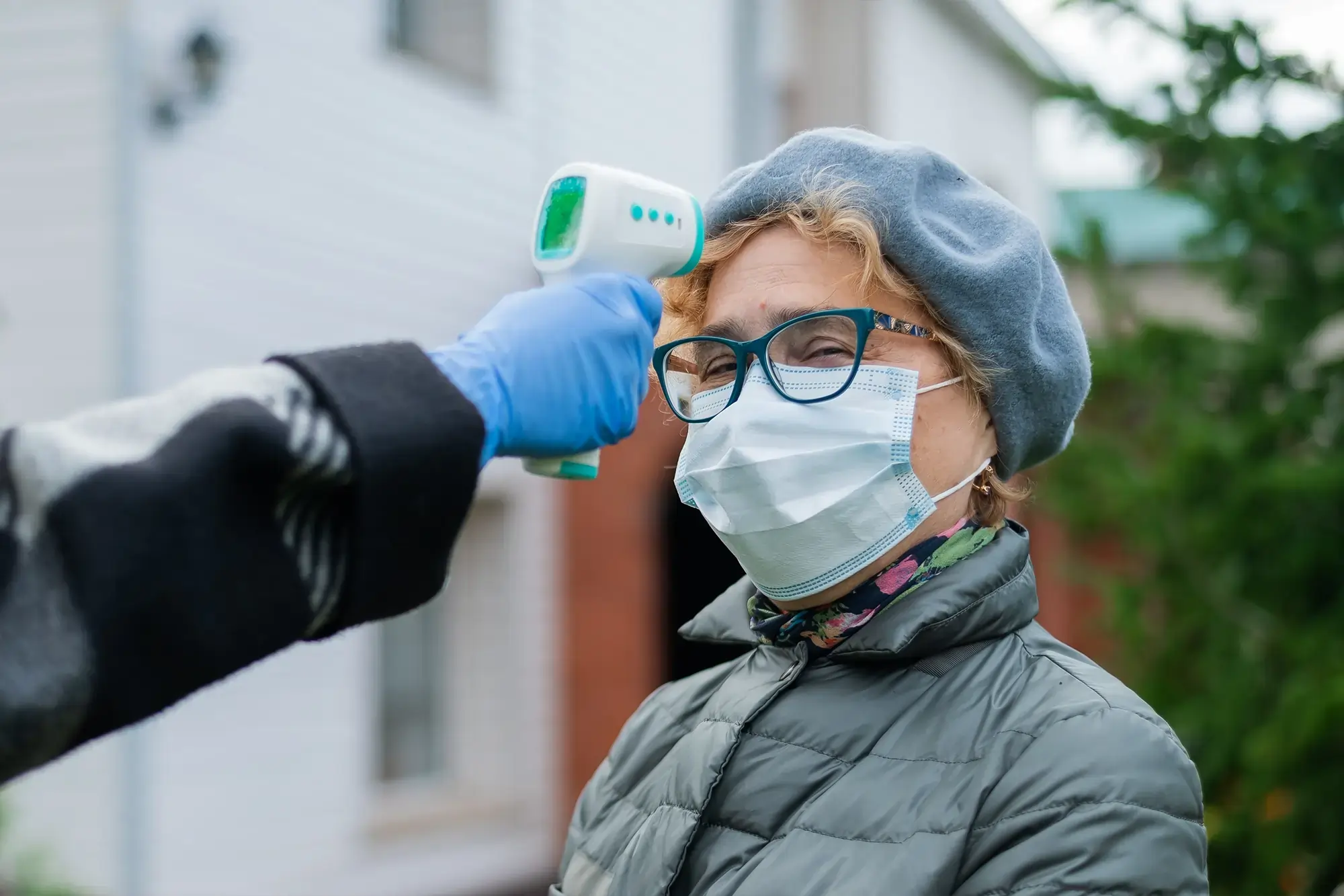 Healthcare worker checking a woman's temperature using a digital infrared thermometer for routine screening.