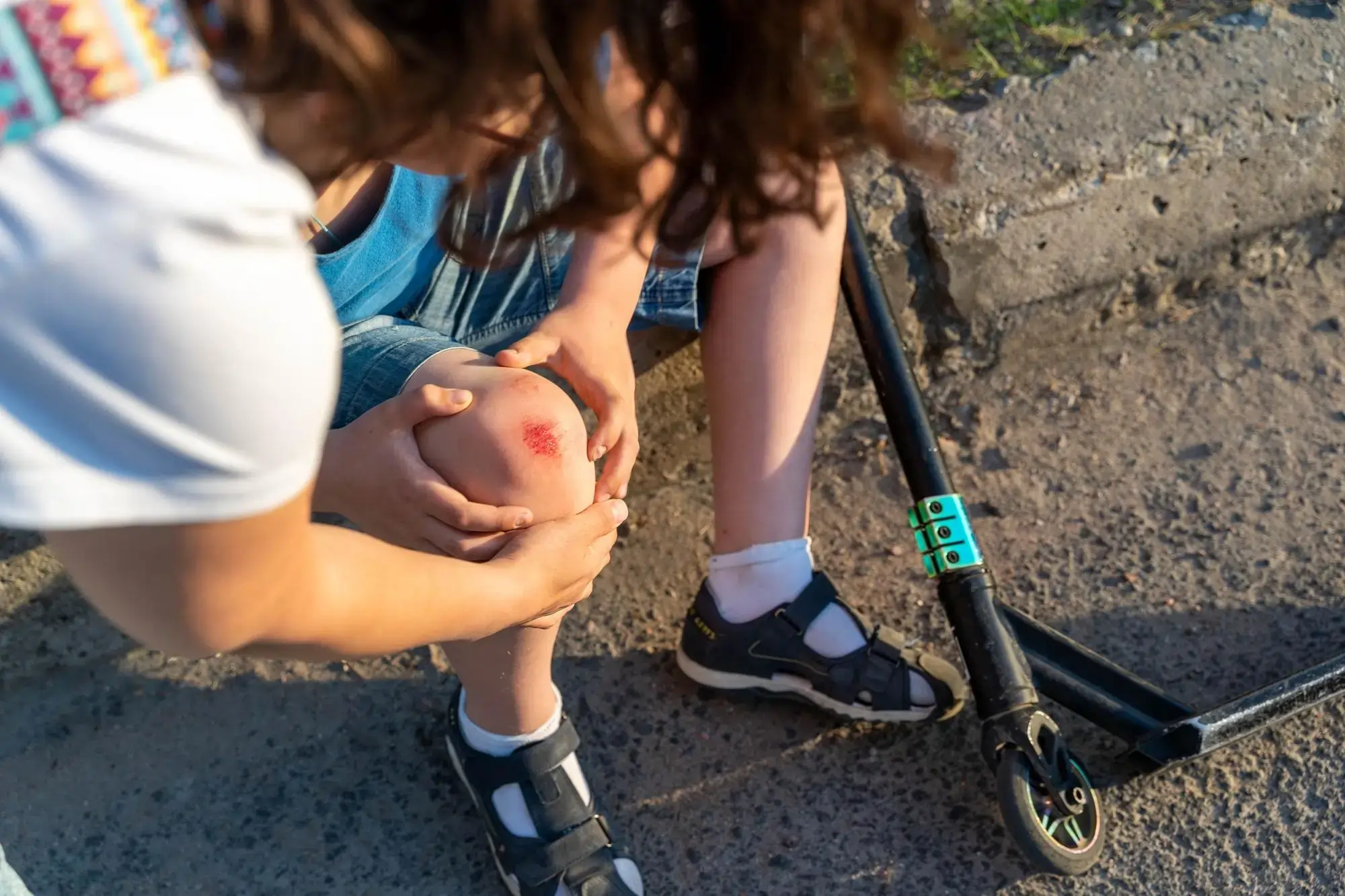 Child with a minor leg joint injury being comforted after getting hurt while playing outdoors.
