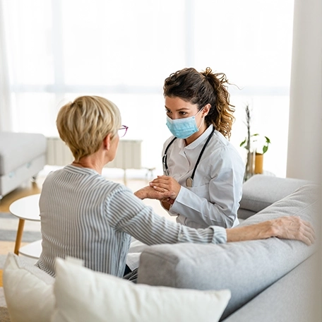 Female doctor holding hands with elderly woman while discussing health concerns.