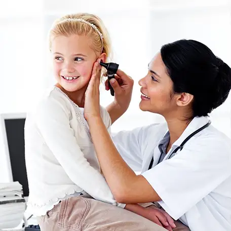 Female doctor examining a teenage girl’s ear during an urgent care visit for ear pain treatment.