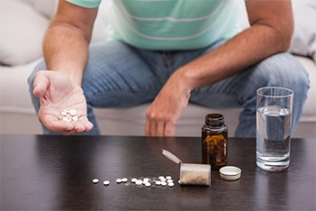 A man sitting at a table with multiple bottles of medication laid out in front of him.