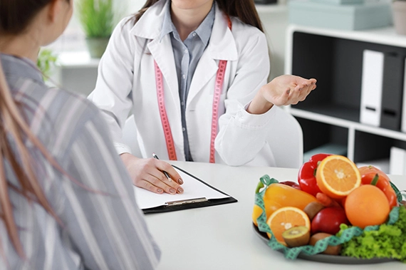 Nutritionist discussing weight loss plan with patient using fruits and vegetables as dietary tools.