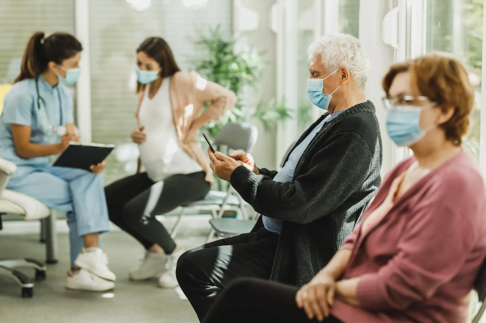 Patients waiting in a clinic lobby while a doctor consults with a pregnant woman.