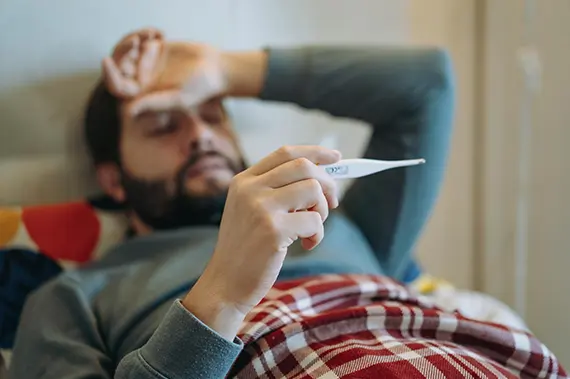 Individual monitoring body temperature with a digital thermometer, a common step when experiencing flu-like symptoms.