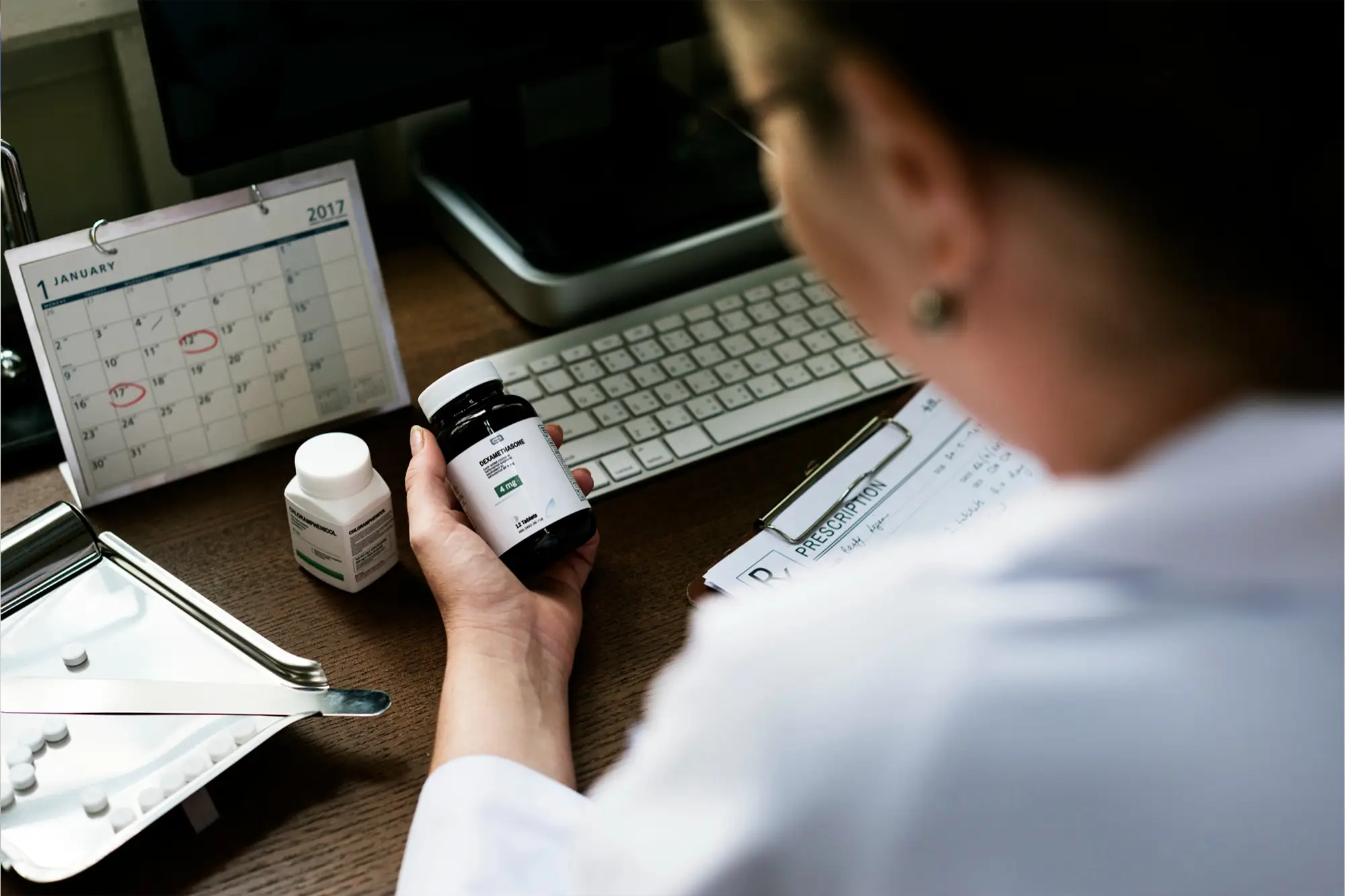 Pharmacist holding a medicine bottle while updating prescription records.