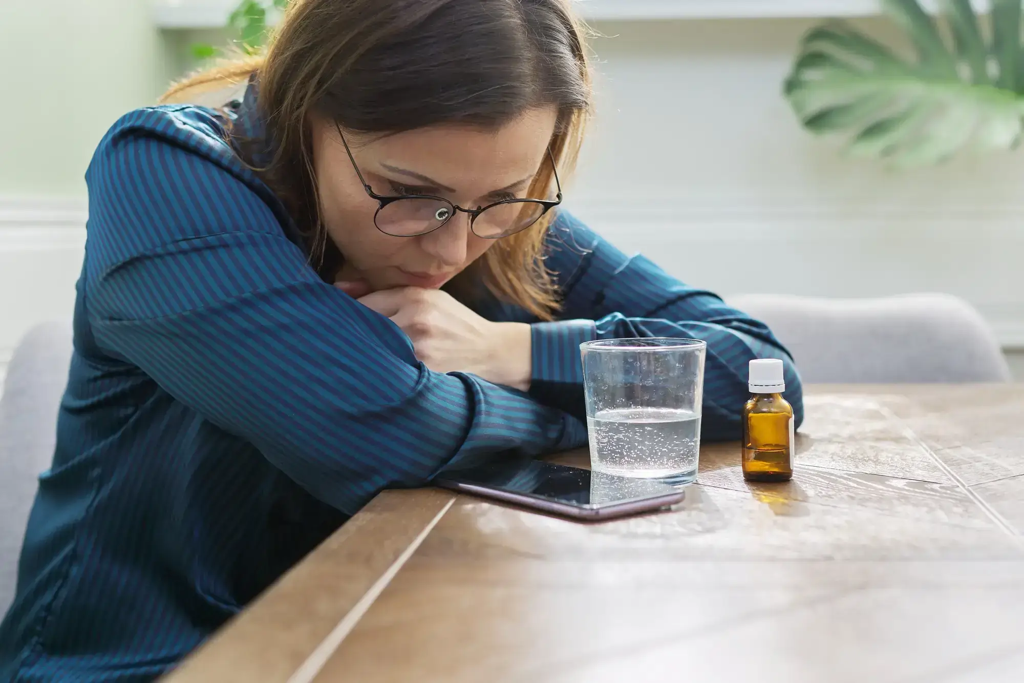 Woman sitting pensively on a chair, looking at a table full of medications, reflecting on her treatment plan.