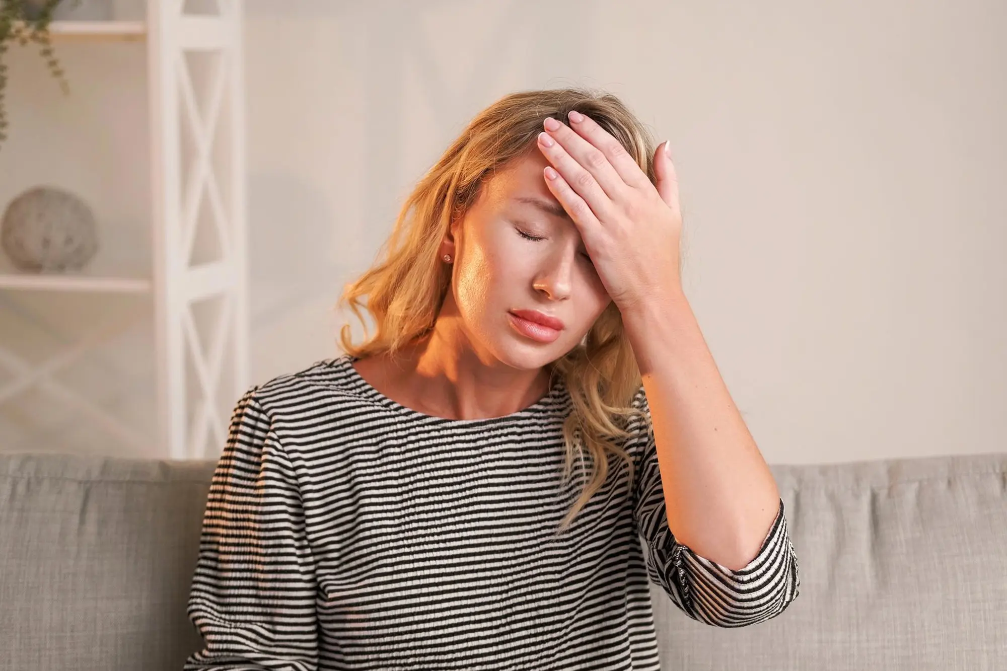 Woman suffering from migraine-related head pain, seeking relief while sitting on a couch.