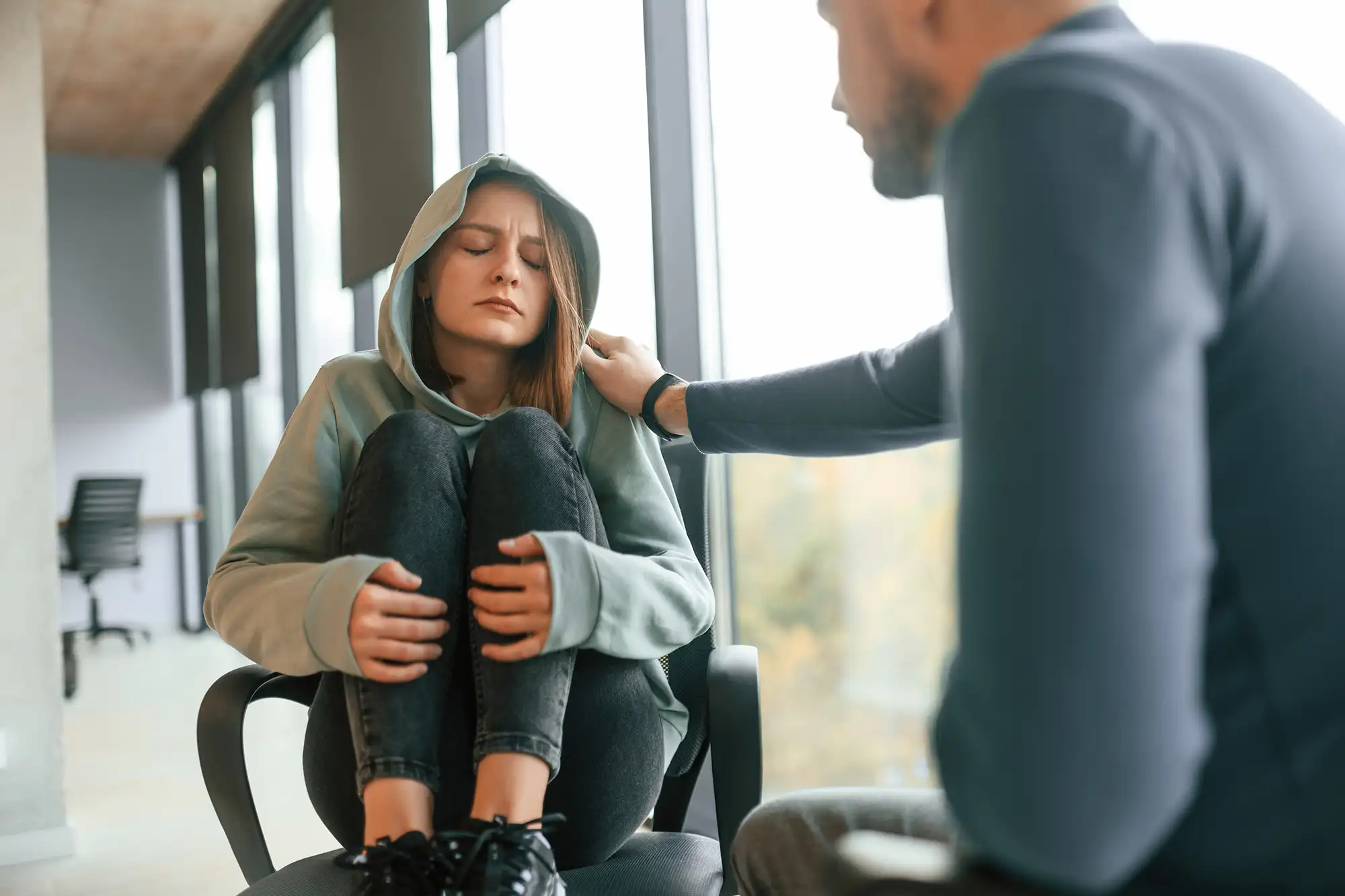 Woman in emotional distress sitting with folded knees, showing trauma symptoms.
