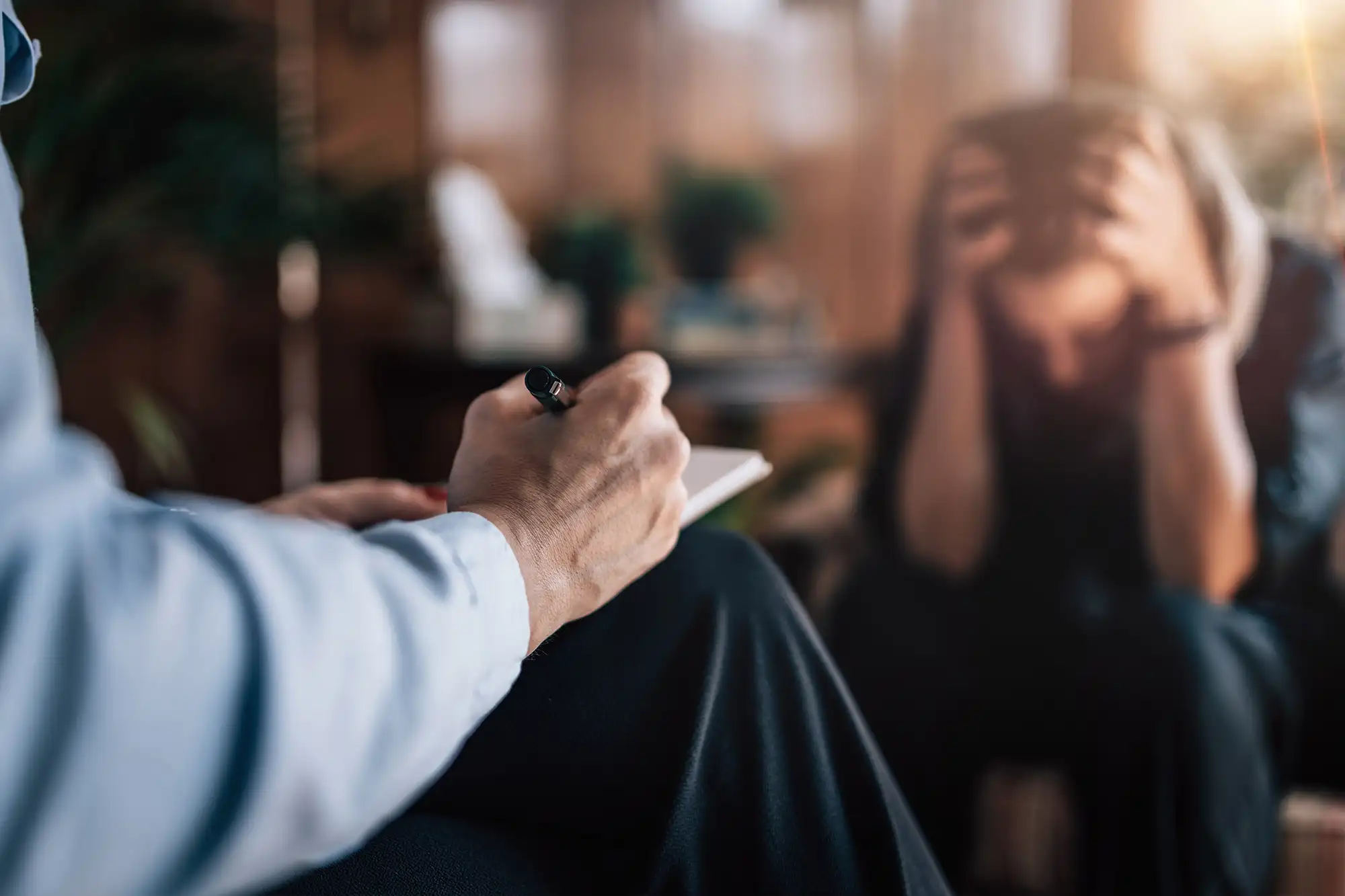 Woman experiencing psychological trauma, sitting with hand on head in a visibly anxious and sad posture.