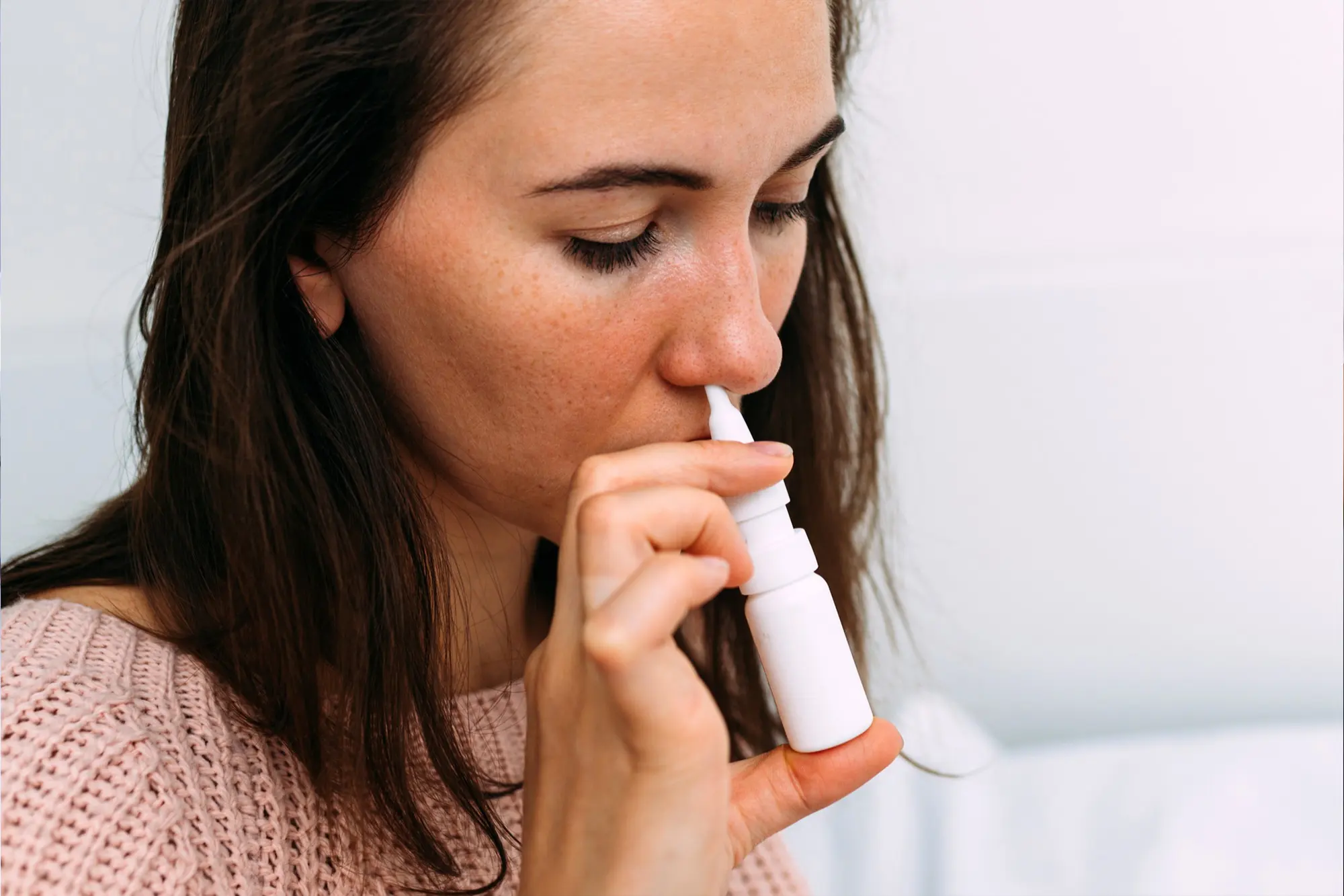 Woman using a nasal spray vaccine as an alternative method for flu prevention.