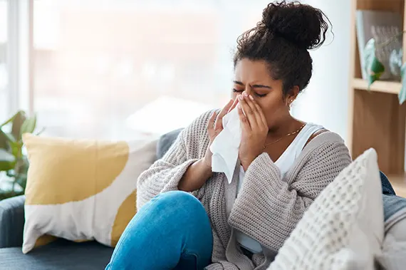 Woman using a tissue while experiencing flu symptoms and a headache.