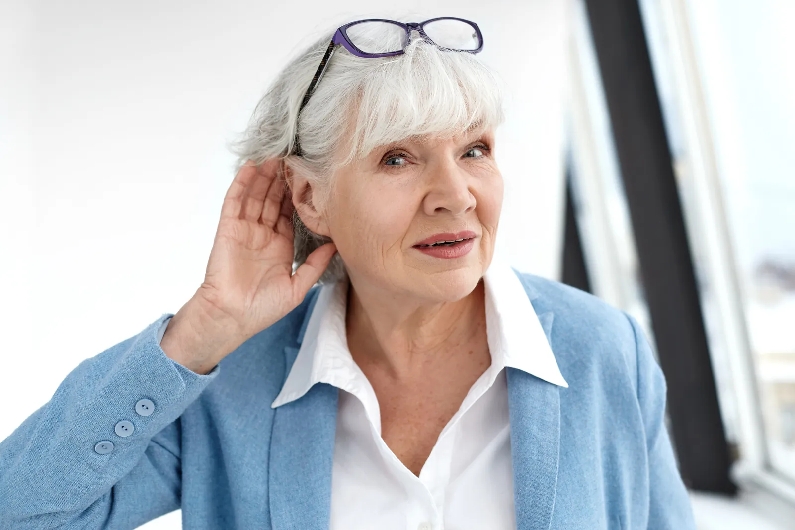 Elderly woman cupping her ear due to hearing difficulty and ear discomfort