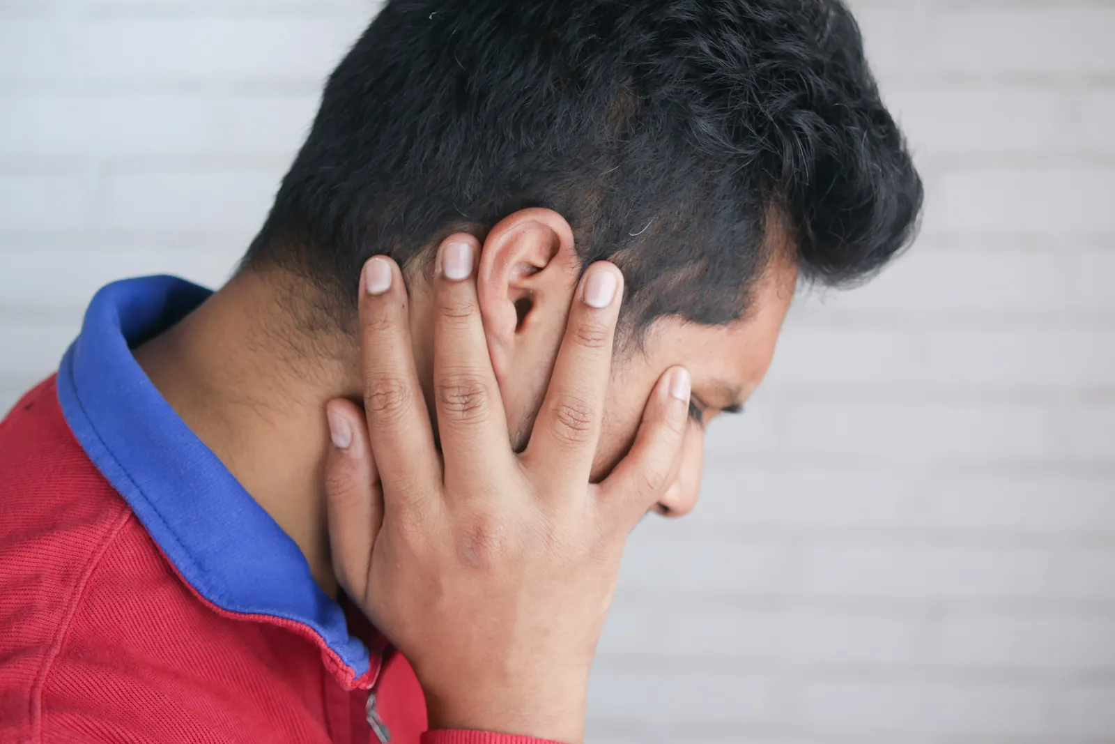 Young man touching his ear in pain against a plain background