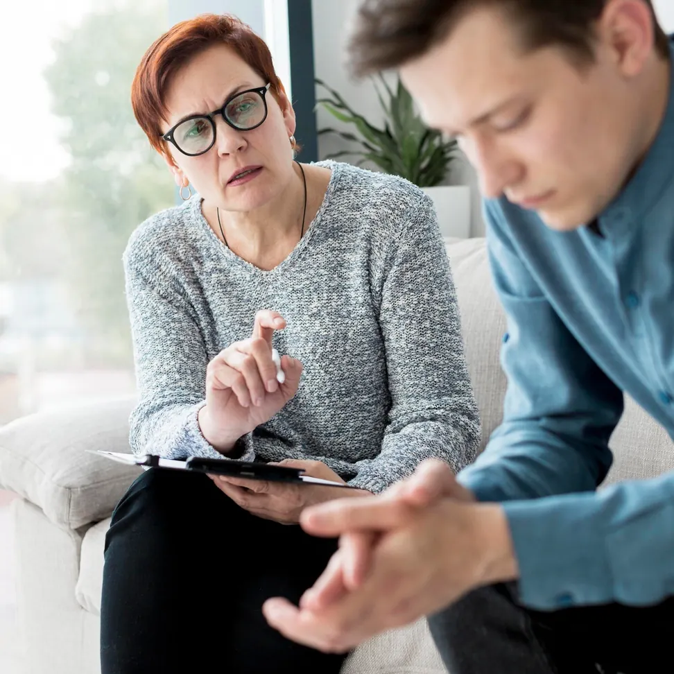 Female counselor with clipboard speaking with a young man who sits with his head down during a private counseling session
