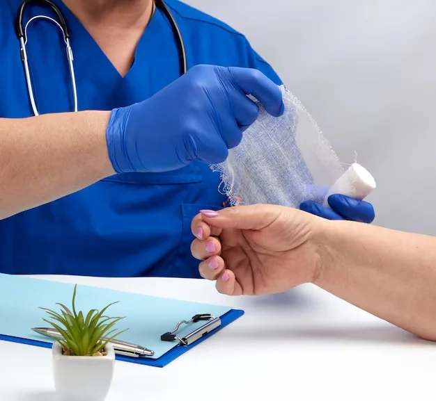 Clinician in blue scrubs and gloves unrolling gauze to bandage a patient's hand