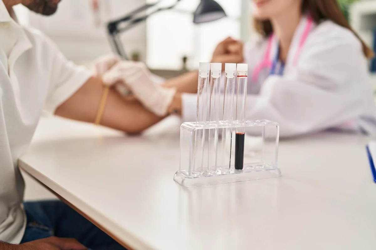 Row of blood collection tubes on a clinic table while a provider draws blood from a patient's arm in the background