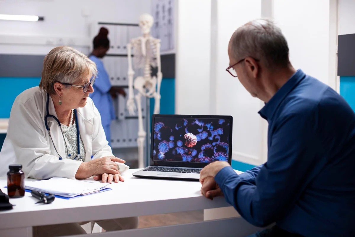 Senior female doctor reviewing health information on a laptop with a male patient during a hormone therapy consultation