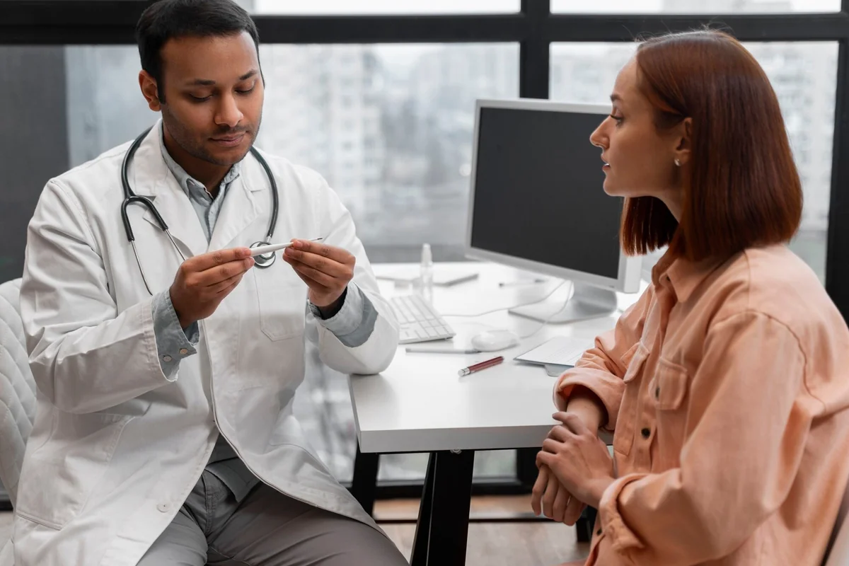 Male doctor holding a thermometer while a female patient listens during a physical evaluation