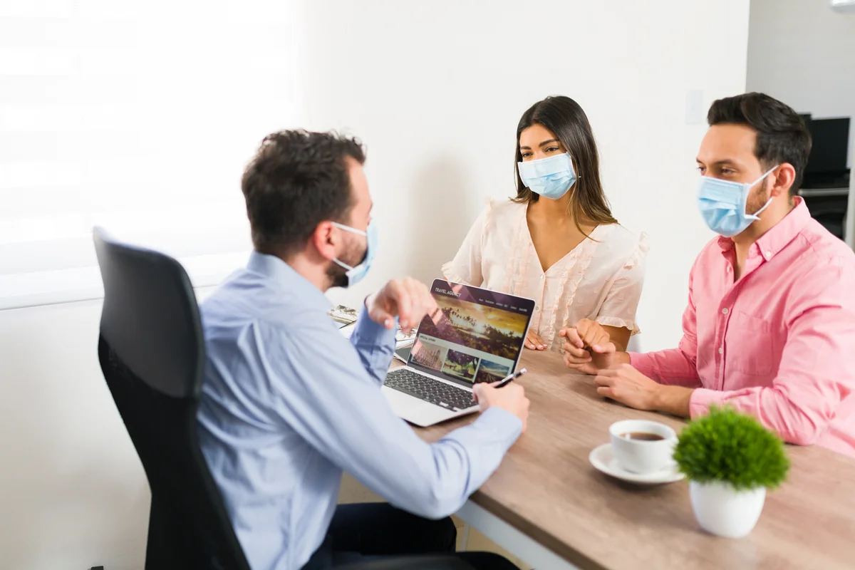 Couple in face masks sitting across a desk from an advisor who shows them a laptop