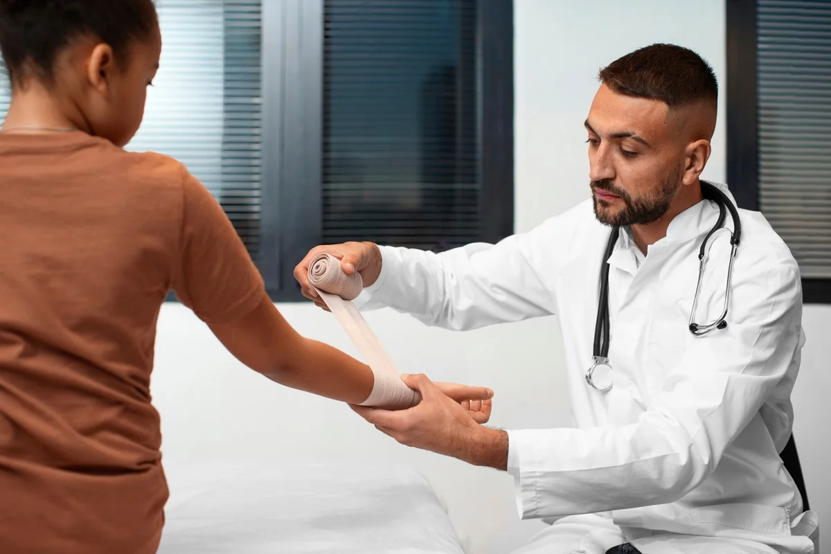 Male doctor wrapping an elastic bandage around a child's forearm in an exam room
