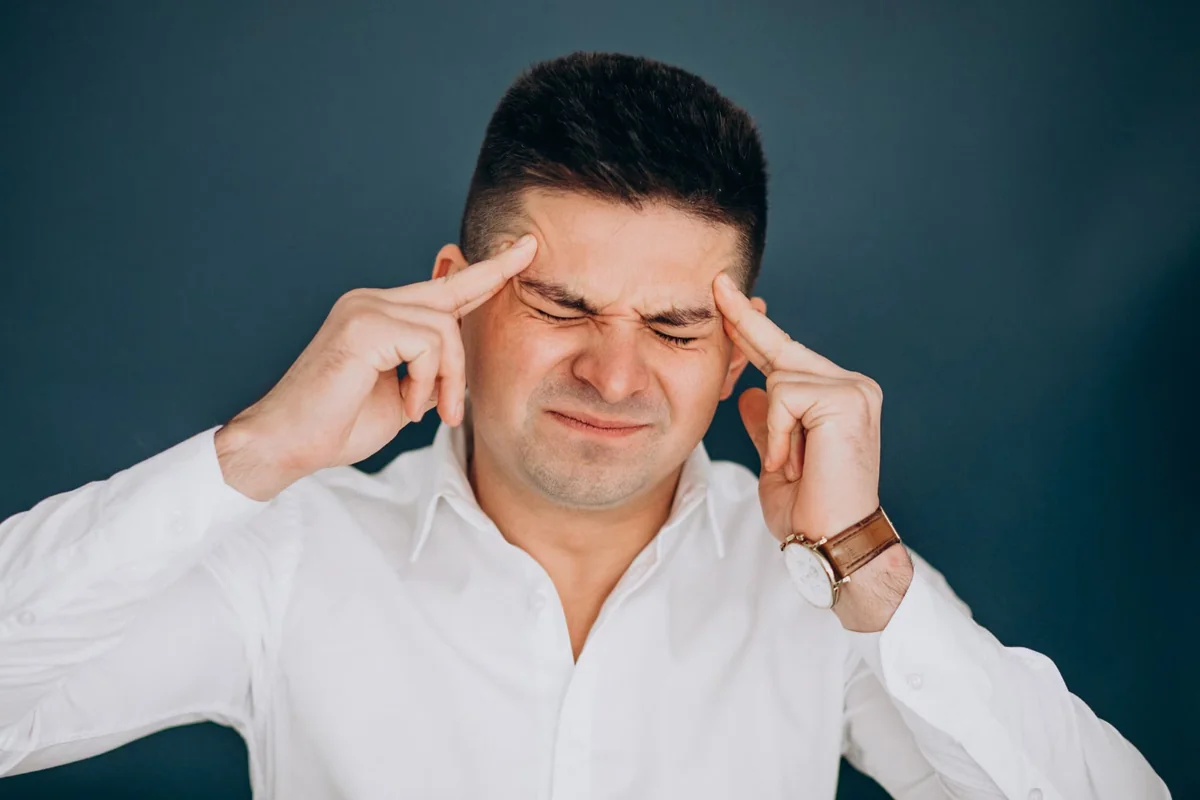 Man in white shirt pressing his temples with a pained expression from a severe migraine headache