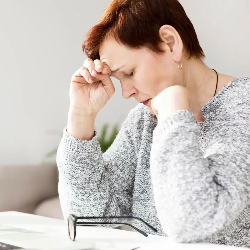 Woman with short hair resting her forehead on her hand at a desk, showing a stress-related headache