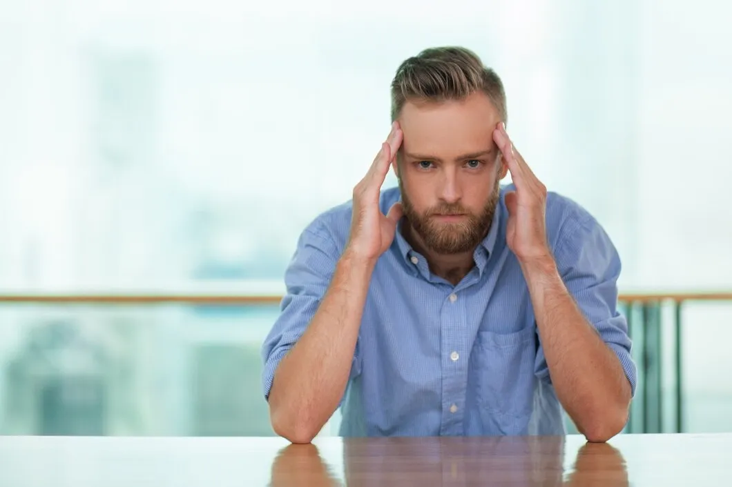 Young man sitting on the floor by a couch with his hand on his forehead from a sudden headache