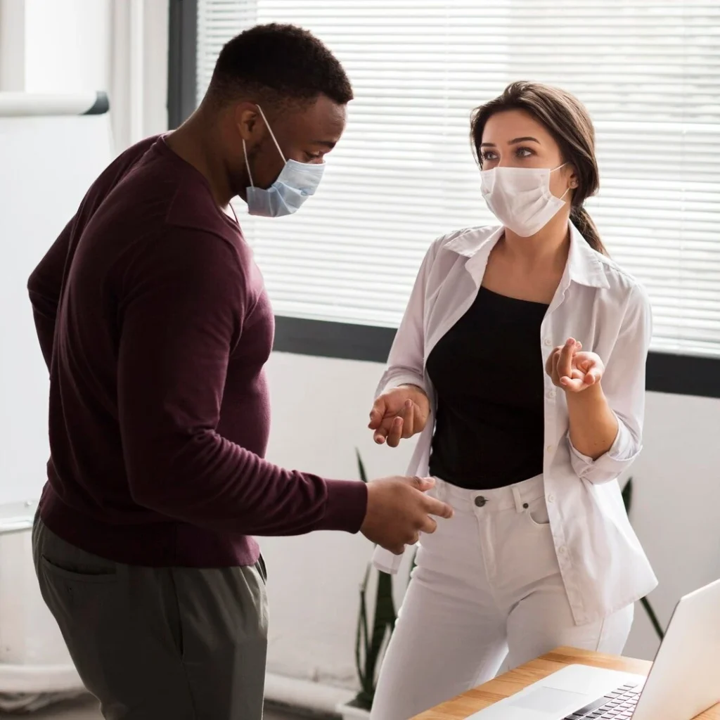 Two adults in face masks talking privately in an office, representing confidential sexual health care in Sanford, NC