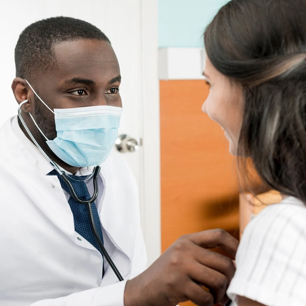 Doctor in a mask using a stethoscope to examine a smiling patient at Rapid Care in Sanford, NC